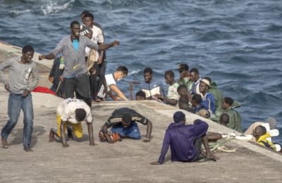 Migrants step off a boat onto a port, assisted by aid workers and officials. Credit: AP photo